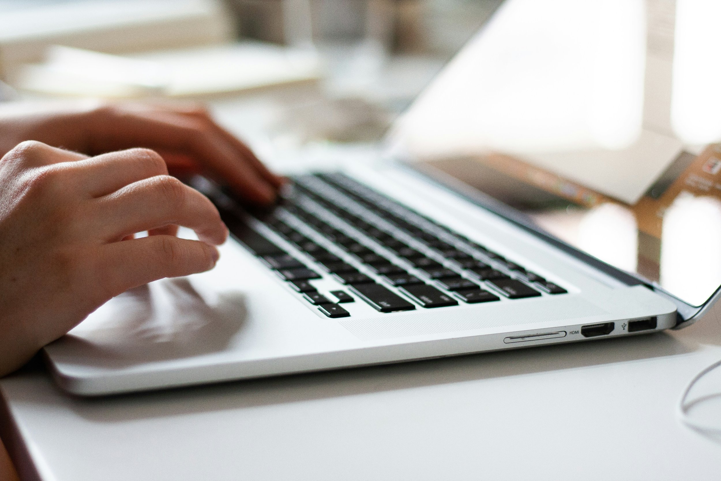 Close-up of hands typing on a laptop keyboard on a white desk.