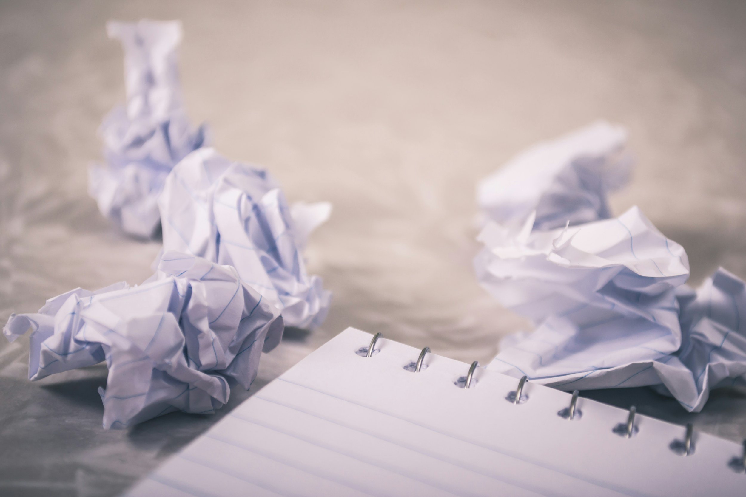 Crumpled sheets of white notebook paper and a lined notepad on a smooth surface.